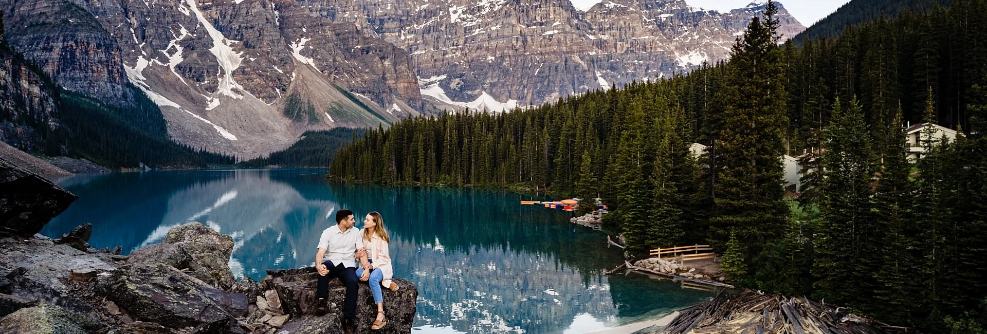 Engaged couple sits on the rock at amazing Moraine Lake against impressive Canadian Rockies.
