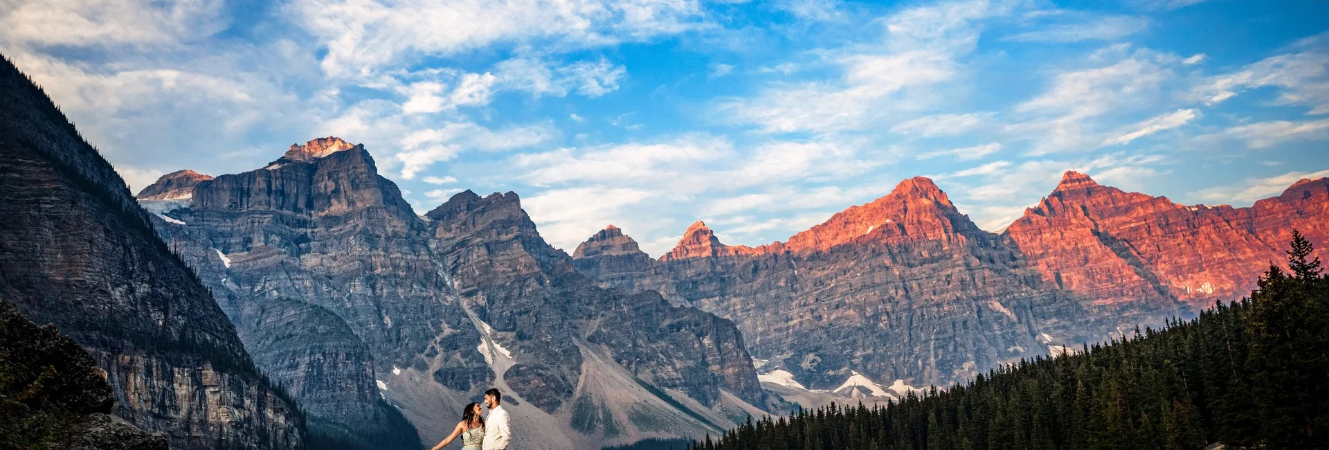 Married couple stand on the edge of the rock at turquoise Moraine Lake in Banff.