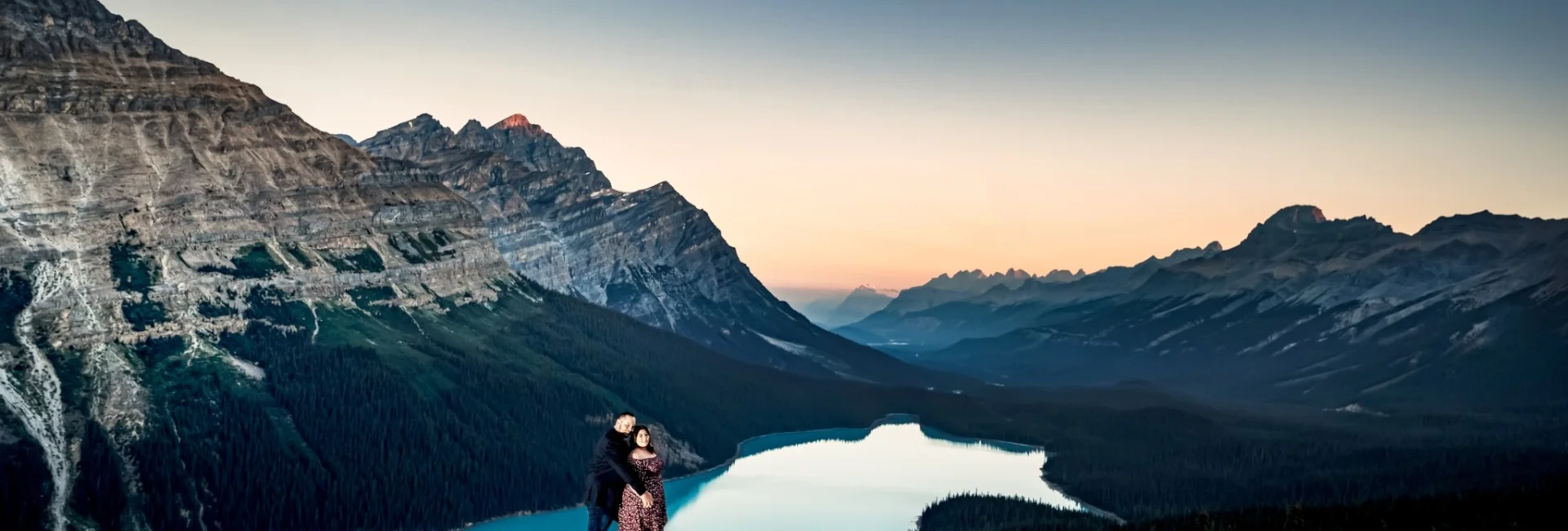 Gentlemen hug his fiance from behind at spectacular location Peyto Lake, surrounded by giant Canadian Rockies