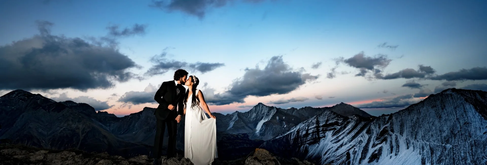 Newlyweds on the of the mountain in Banff posing to Banff Wedding Photographer. Against them stunning view of the Canadian Rockies.