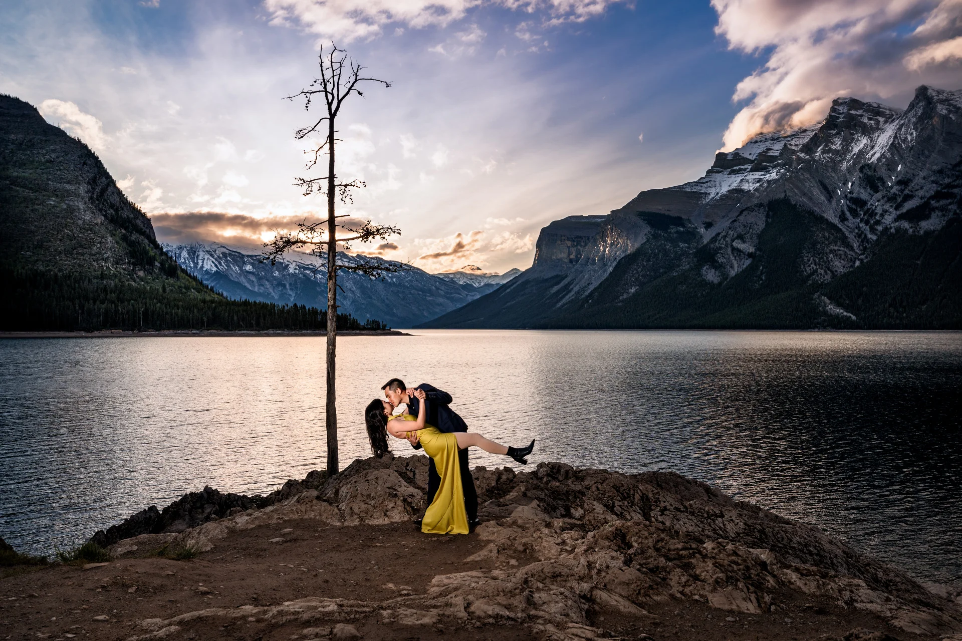 Couple in love dance at Minnewanka Lake during stunning sunrise.
