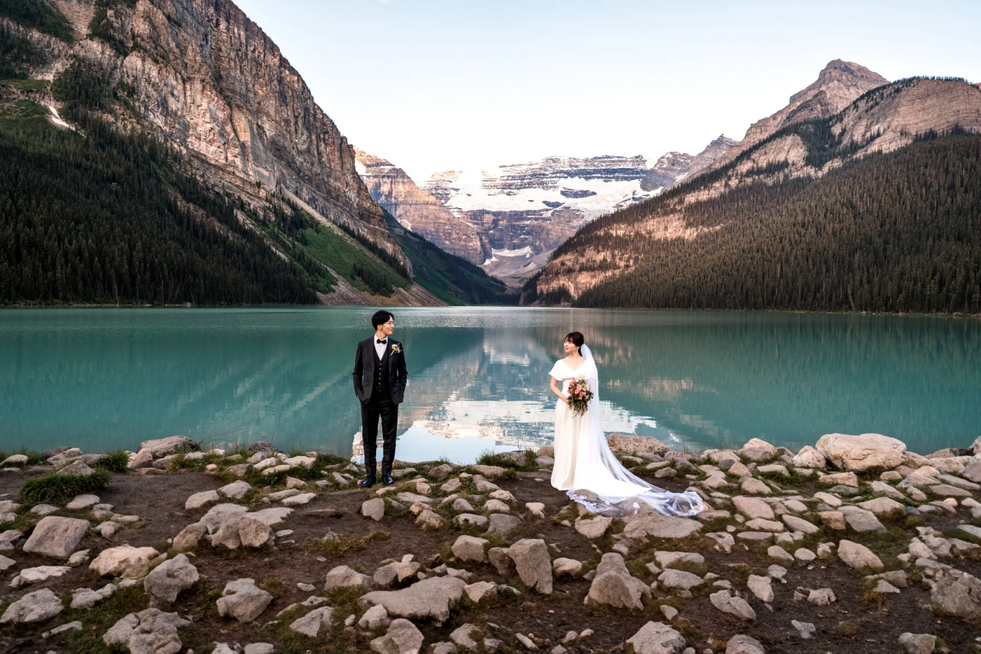 Bride and groom look at each other from a distance at the stunning location of Lake Louise in the Canadian Rockies.