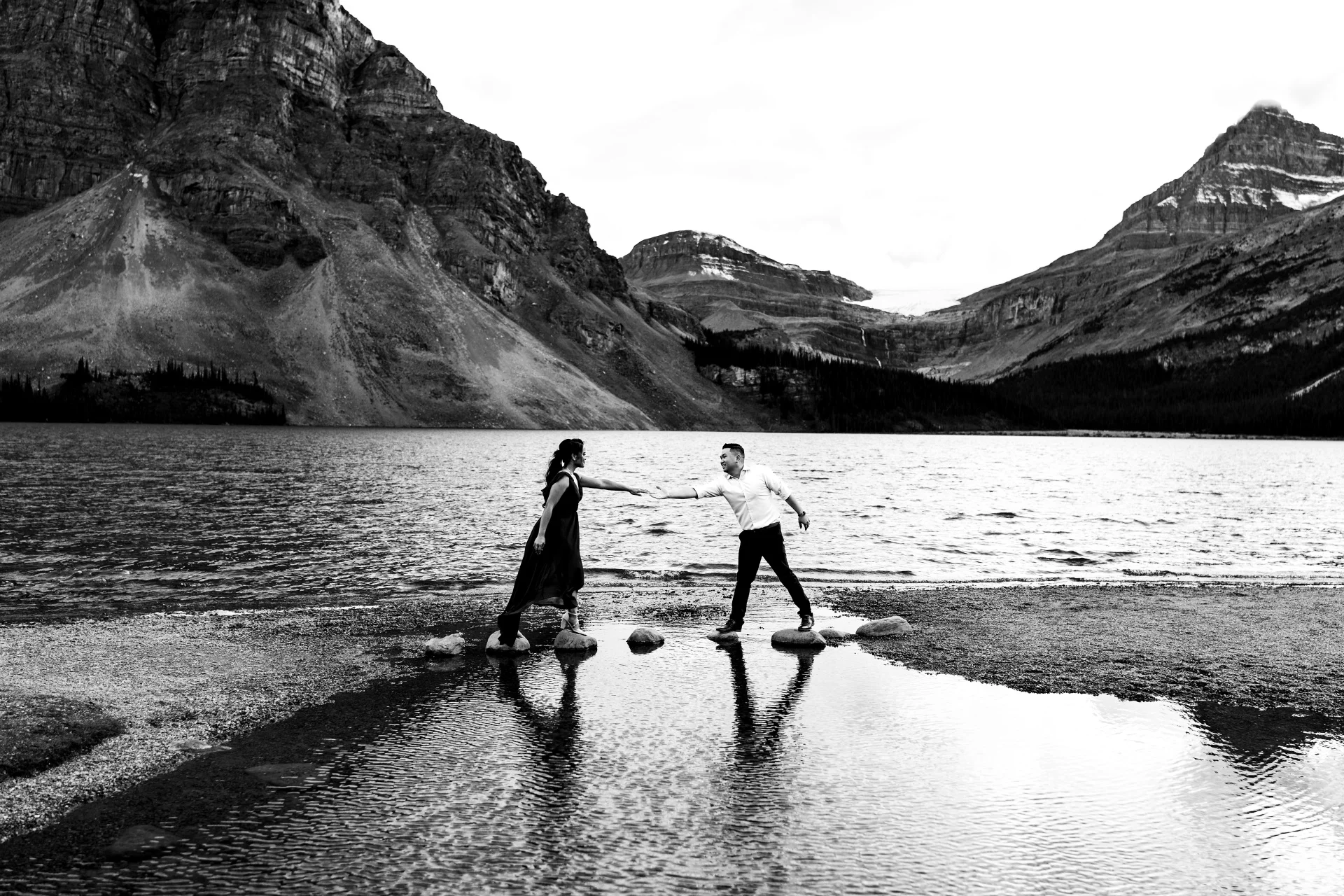 Engaged couple trying to walk on the rocks at Bow Lake during their engagement session