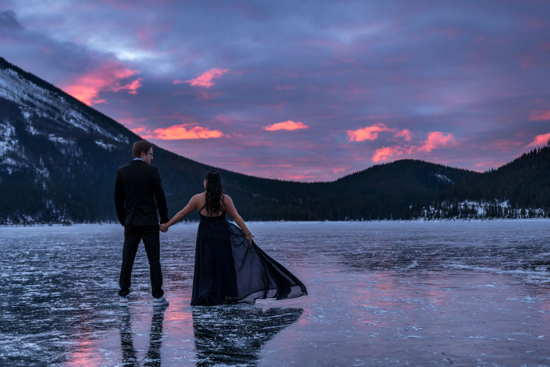Engaged couple is looking at the red sunrise in the mountains. Engagement photo session in Banff.