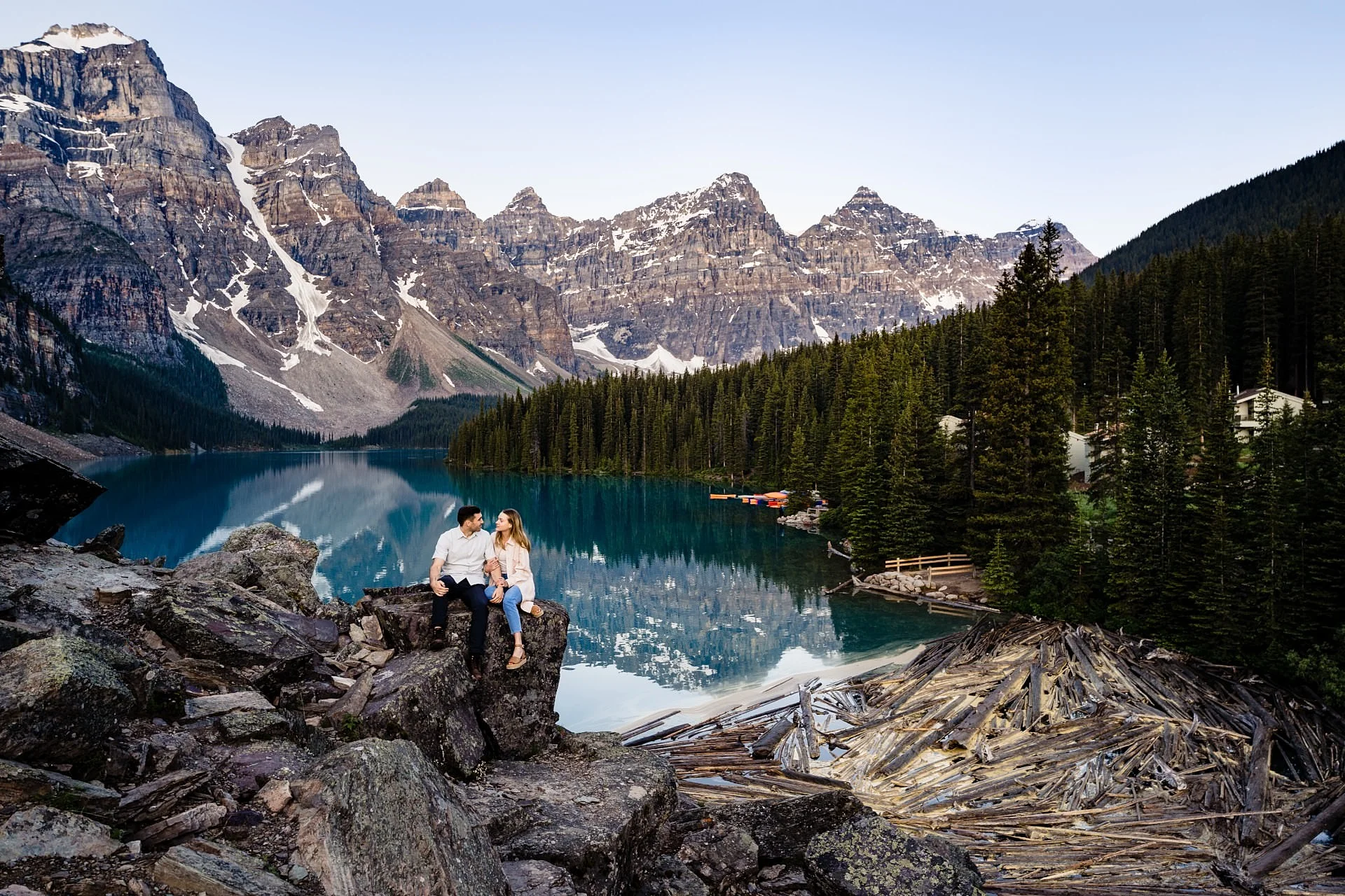 Engaged couple sits on the rock at amazing Moraine Lake against impressive Canadian Rockies.