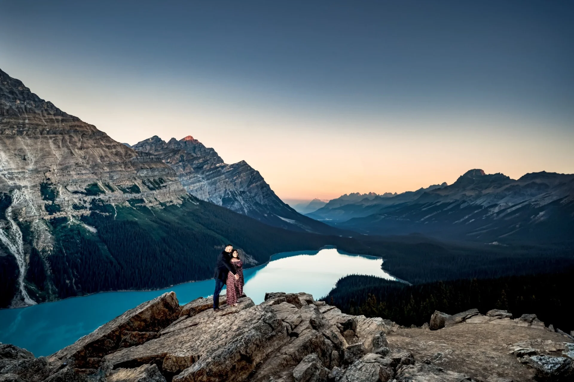 Gentlemen hug his fiance from behind at spectacular location Peyto Lake, surrounded by giant Canadian Rockies