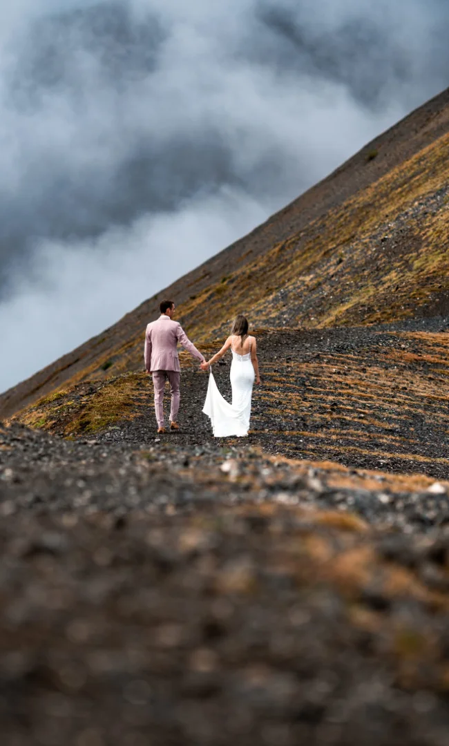 Bride and groom hold their hands and walk at the mountain ridge in the Canadian Rockies.