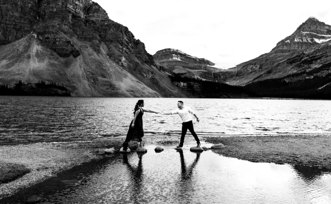 Engaged couple trying to walk on the rocks at Bow Lake during their engagement session