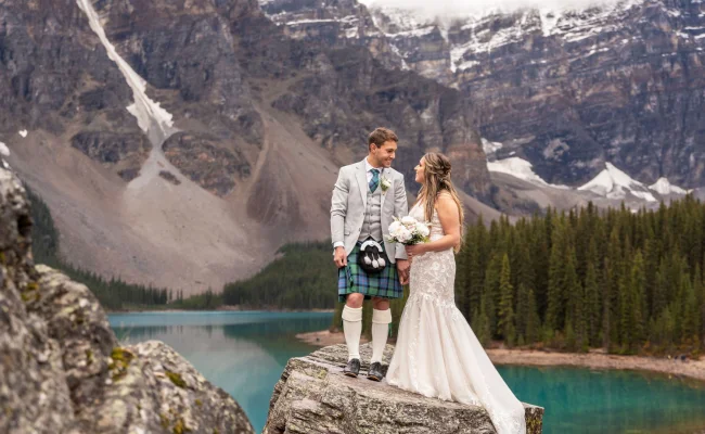 Newlyweds look at each other surrounded by Rocky Mountains at Moraine Lake in Banff.