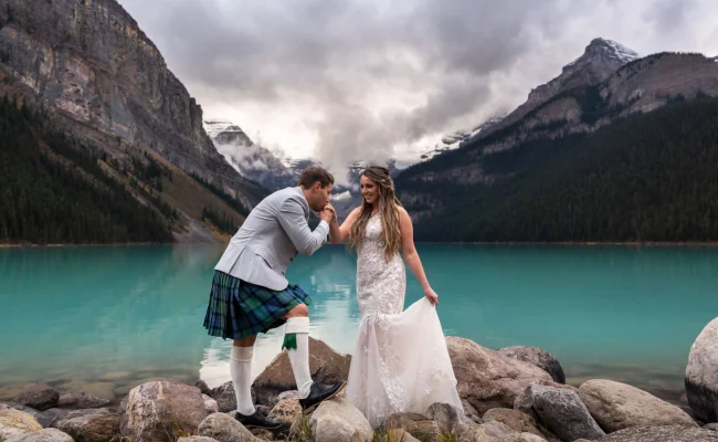 Groom kissing the bride's hand during elopement ceremony at Lake Louise.