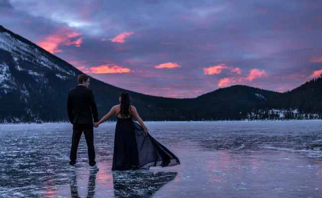 Engaged couple is looking at the red sunrise in the mountains. Engagement photo session in Banff.