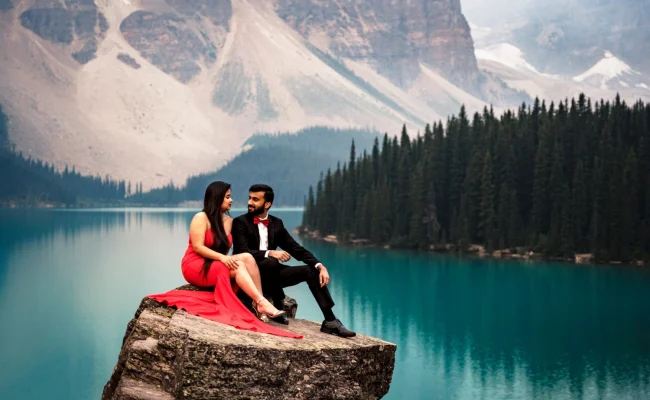 Engaged people sitting at the giant rock and look at each other during Moraine Lake engagement photo session with 4Eyes Photography Canada.