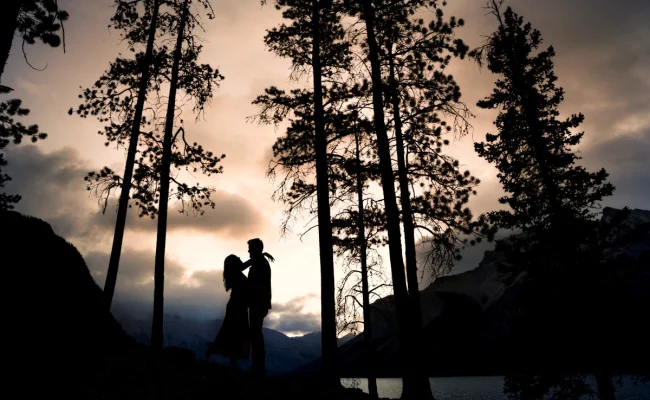 Engaged couple look at each other at Minnewanka Lake during the sunrise