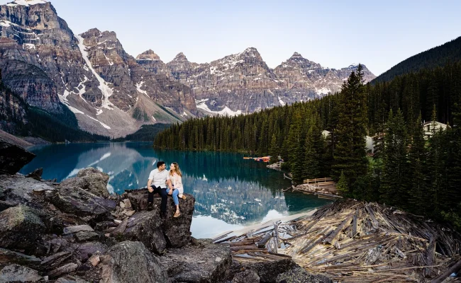 Engaged couple sits on the rock at amazing Moraine Lake against impressive Canadian Rockies.