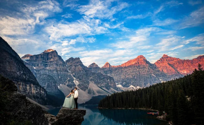 Married couple stand on the edge of the rock at turquoise Moraine Lake in Banff.