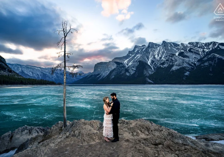Winning Engagement Photograph from Banff. Couple standing by the frozen Minnewanka Lake in a hug.