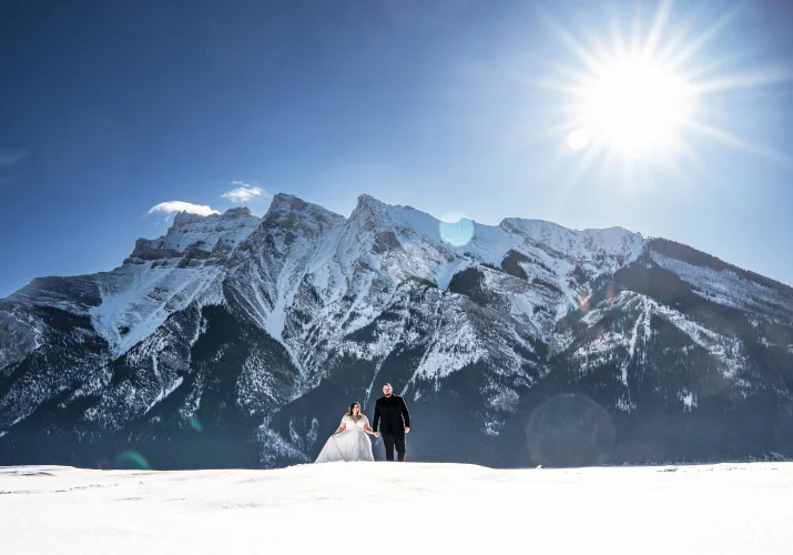Newlyweds walk at the frozen lake in Banff. Behind them tremendous mountain covered with snow.