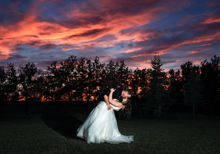Groom dips the bride while they dance during stunning sunset in Calgary.