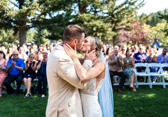 Bride and groom share a first kiss at the Calgary Wedding Ceremony. All the guests clapping their hands