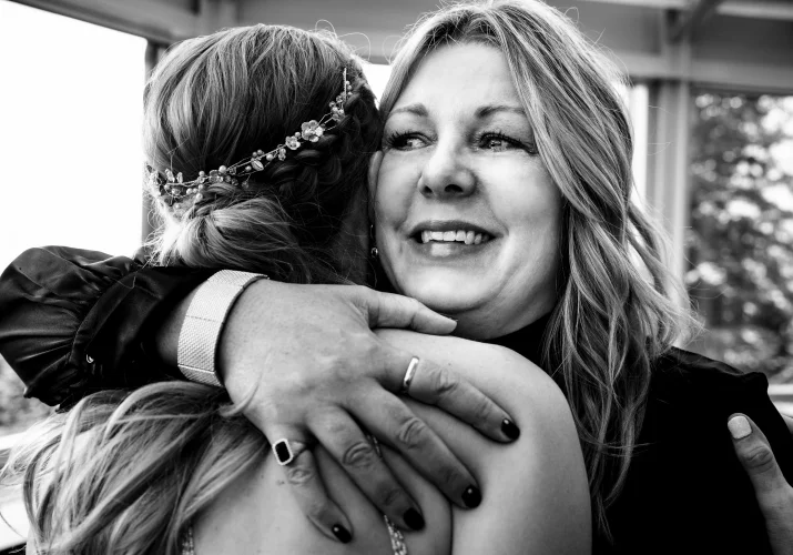 Sister of the groom hugs the bride with tears in her eyes.