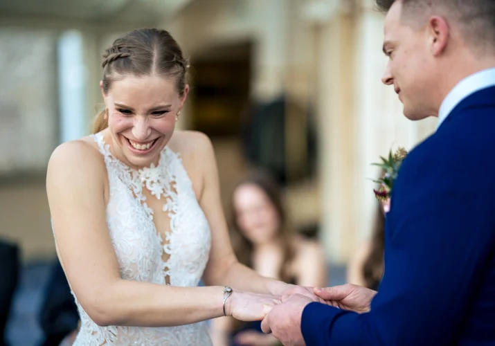Bride and groom hold their hands while the bride laughs during groom's speech.