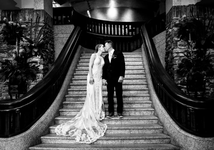 Bride and groom share a kiss at the staircase at Fairmont Banff Springs.
