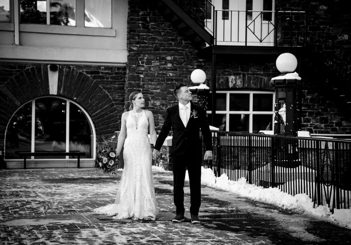 Newlyweds walk holding their hands in front of the Fairmont Hotel Springs in Banff.
