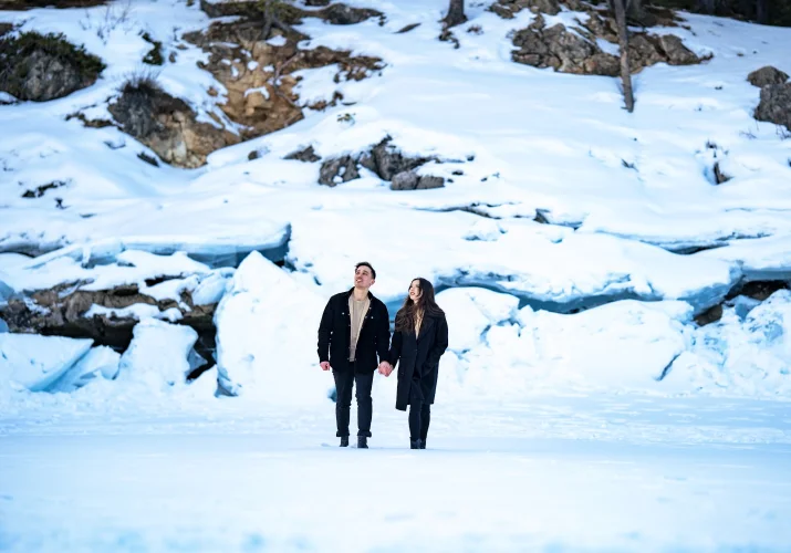 Couple lovers in black walking at the frozen lake behind them a wall of frozen snow.