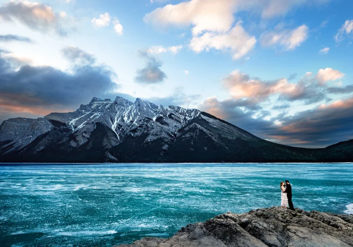 Tiny people standing at the rock at the frozen Minnewanka Lake in the mountains.