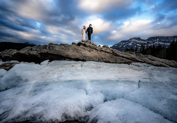 Man and woman hold their hands while standing at the giant rock. Above them colorful clouds.