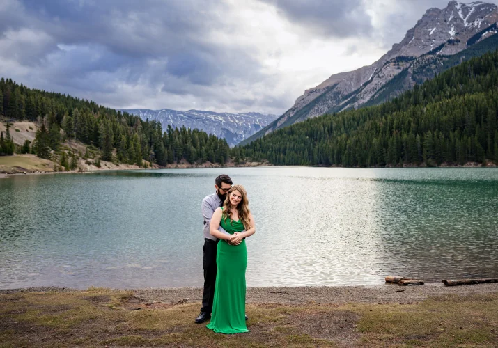 Romantic photograph of the man hugging his fiancee in a green dress. Photograph at Two Jack Lake in Banff.