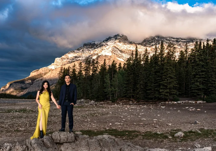 Lady in a yellow dress and her fiancee stand at the rock in Banff during an engagement session performed by the best Banff Wedding Photographer.