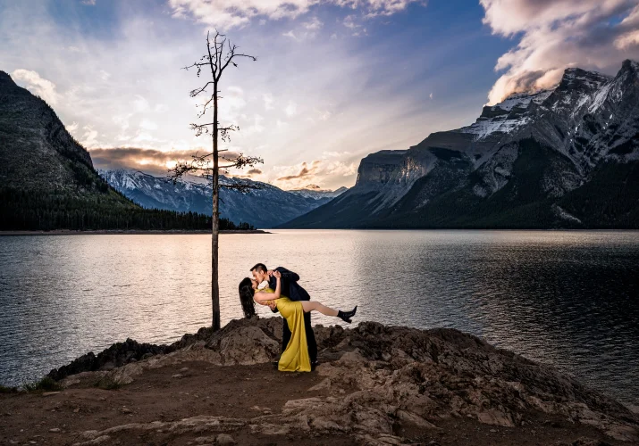 Engaged couple dance during sunrise at Minnewanka Lake in Banff. Behind them stunning view of the Canadian Rockies.