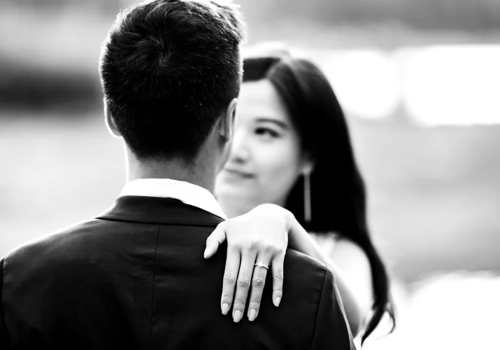 Photograph in Black and white of the couple looking at each other. Her hand on his arm with the big engagement ring.