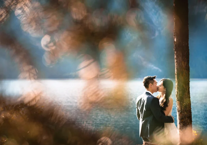 Engaged couple share a kiss by the Minnewanka Lake . Photo taken by Banff Wedding Photographers.