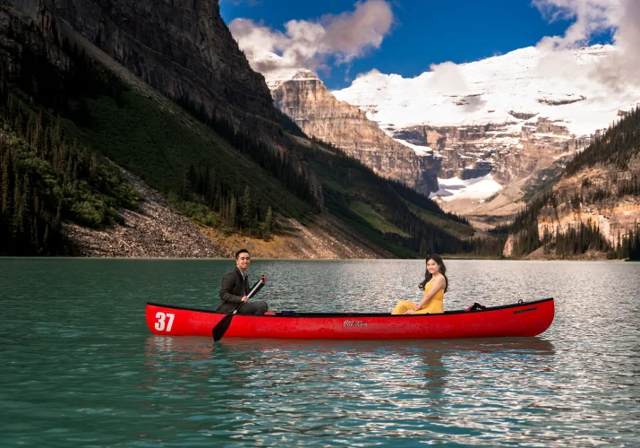 Lady in a yellow dress and a gentleman in a suite paddling in the red canoe at Lake Louise.