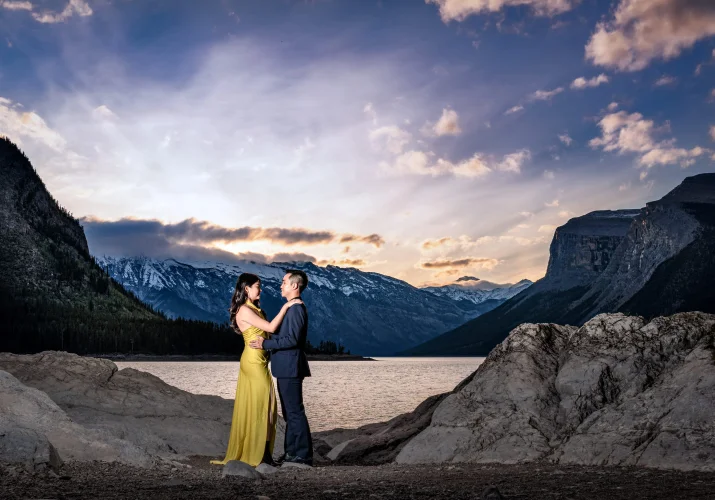 Stunning Photograph at Minnewanka Lake taken by Banff Wedding Photographers of the couple looking at each other while hugging during stunning sunrise.