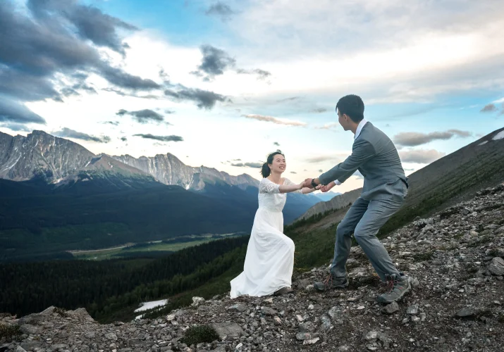 Groom helps the bride climb the mountain.