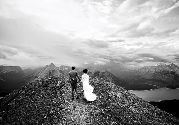 Photograph in black and white in the mountains on the bride and groom from behind.