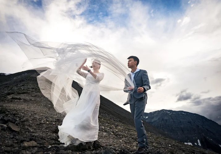 The groom helps the bride to put back her veil during windy day in the mountains.