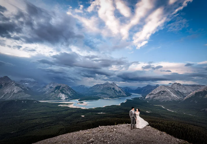 Stunning photograph taken by Banff Wedding Photographer if the newlyweds standing in a hug at the edge on the mountain.