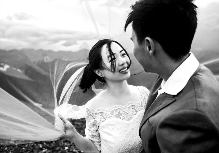 Black and white photograph under the veil of the bride and groom looking at each other.