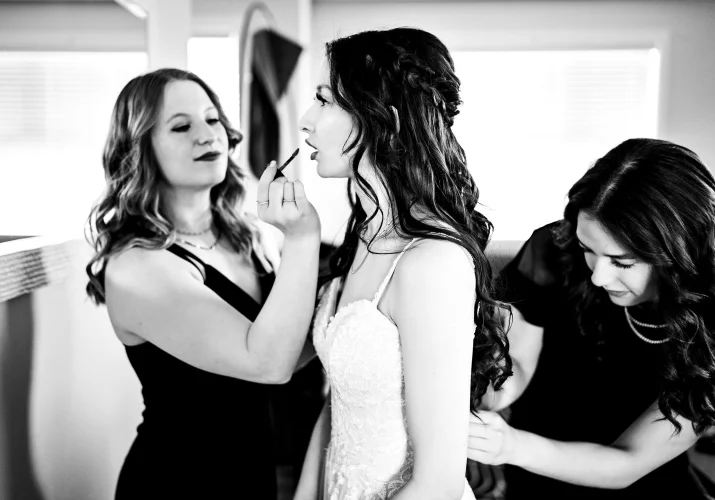 Bridesmaid help the bride to fix her make up and zip up the wedding dress