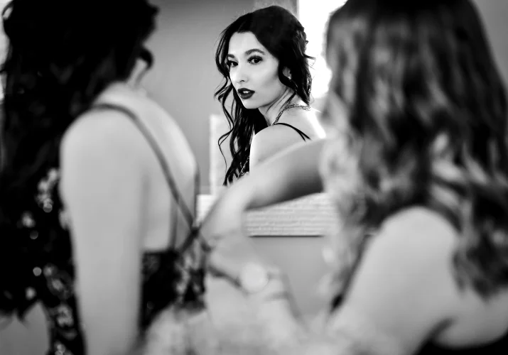 mirror reflection of the bride looking in the mirror while maid of honour fixes her wedding dress