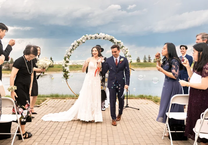 Bride and groom walking down the aisle in Calgary while wedding guests blow soap bubbles.