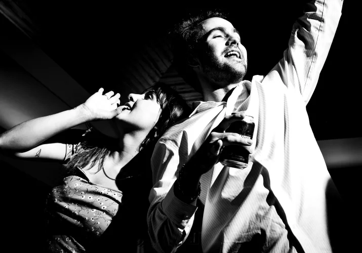 Man with the drink in his hand and a woman making fun of him, pretending that she drinks as well.