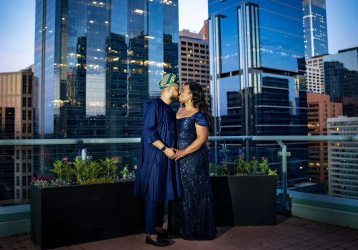 Newlyweds dresser in a traditional Nigerian attire share a kiss on the balcony. On the background the view on the city of Calgary.