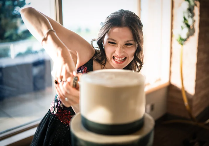The bride tries to cut the wedding cake, she makes a funny faces.