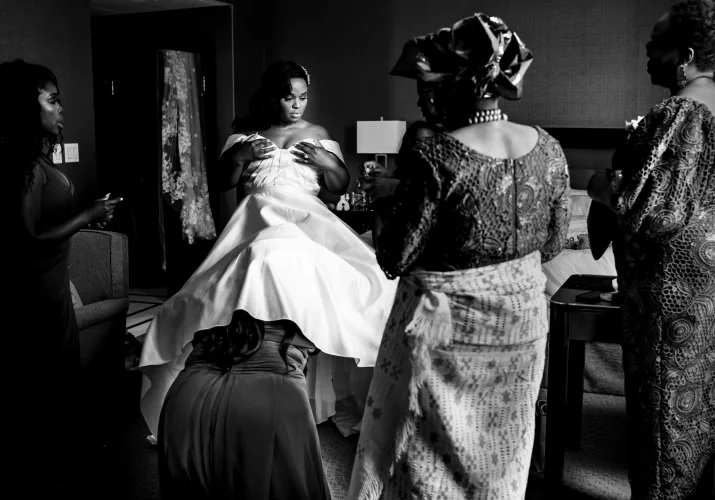 Maid of honour under the bride's wedding dress. Mother of the bride look at them.