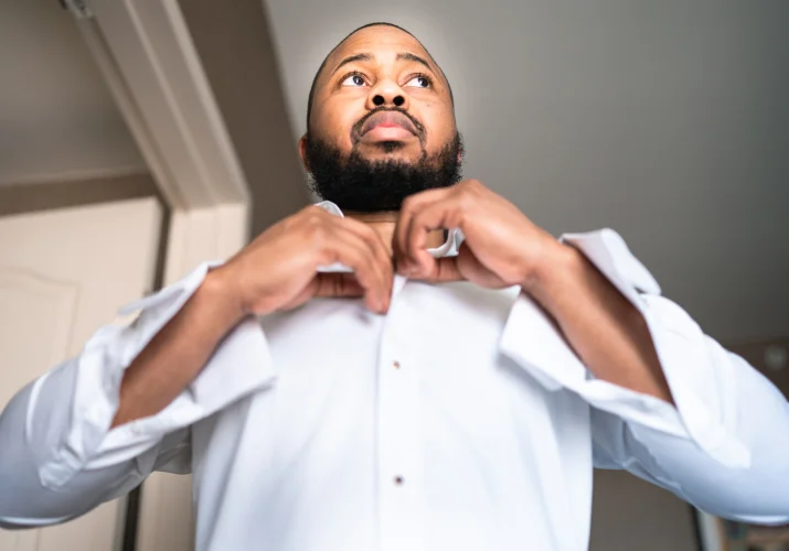 The groom buttons up his shirt before wedding ceremony in Calgary.